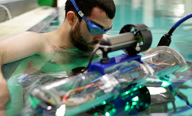[Picture] Peter guides the AUV in the water and holds it steady for calibration.